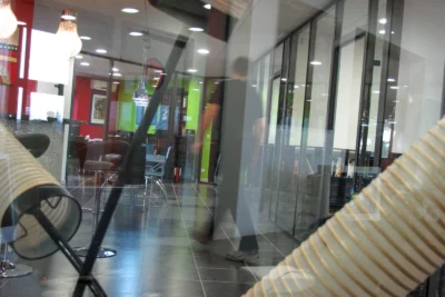 Un bureau moderne avec des murs colorés et des cloisons vitrées, où un jeu de reflets et de transparence superpose un homme en mouvement avec l’environnement, créant un effet visuel presque fantomatique. - Agrandir l'image 23 sur 28, fenêtre modale